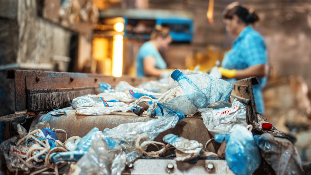 Plastic garbage on a conveyor belt at waste recycling factory. Workers on the background